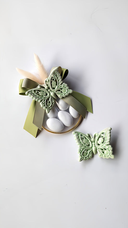 Bomboniera per matrimonio o battesimo con farfalla in ceramica smaltata verde, tulle con confetti bianchi, cerchio dorato e fiocco elegante, realizzata a mano in stile naturale.
